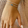 Blue evil eye bangle worn with another bracelet against a knitted top
