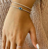 Blue evil eye bangle worn with another bracelet against a knitted top