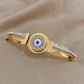 Front detail of a gold tone bangle with a round blue eye, clear halo and split band