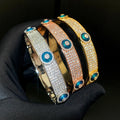 Three evil eye bangles with rows of clear accents and blue eye discs held against a black glove