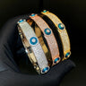 Three evil eye bangles with rows of clear accents and blue eye discs held against a black glove