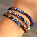 Three beaded bracelets worn together, with blue, cream-spotted and brown beads surrounding blue eye details