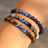 Three beaded bracelets worn together, with blue, cream-spotted and brown beads surrounding blue eye details