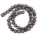 Very dark translucent beads with white eye rings and dark centers, arranged in a loop