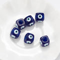Blue cube evil eye beads spaced across a white dish