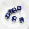 Blue cube evil eye beads spaced across a white dish