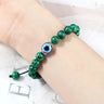 Green bracelet with dark striped beads and a blue eye shown on a wrist