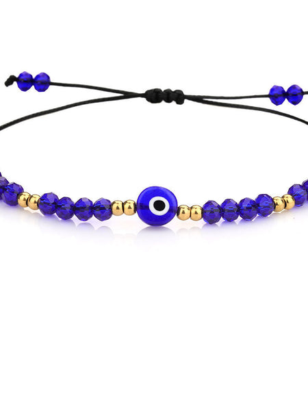 Deep blue faceted bead bracelet with a round blue eye, gold tone spacers and black cord on a white background.