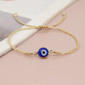 Blue evil eye bracelet with double gold tone cord and round beads, shown at an angle
