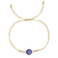Blue evil eye bracelet with double gold tone cord and beaded tails on a white background