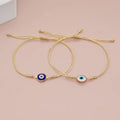 Blue and white evil eye bracelets with double gold tone cords and beaded tails on a pink background
