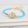 Sunburst evil eye bracelet with a light blue braided cord, blue-on-white eye, and multicolored accent border