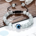 Translucent white bead bracelet with a blue eye and black cord, shown at an angle on a wooden surface