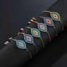 Six chain bracelets with almond-shaped eyes, turquoise or dark blue centers, and gold tone, silver tone or rose gold tone chains on a black display.