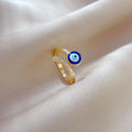 Angled view of a gold tone blue evil eye ring showing the dimpled band and curved row of clear accents