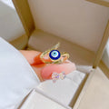 Gold tone blue evil eye bypass ring held between fingers, showing the clear accents and open front