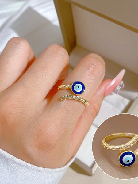 Gold tone blue evil eye ring worn on a finger, with an inset close-up of the open band