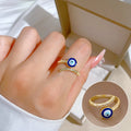 Gold tone blue evil eye ring worn on a finger, with an inset close-up of the open band