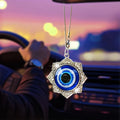 Blue evil eye ornament surrounded by a silver tone floral star frame with scroll details, shown hanging in a car interior.
