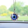 Blue evil eye car ornament in a silver tone floral star frame with pointed petals and scroll details, hanging before a windshield.