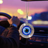 Round blue evil eye ornament with a silver tone Greek key frame, shown hanging in a car interior.