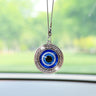 Round blue evil eye car ornament with a silver tone Greek key border, shown hanging in front of a windshield.