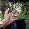 Round blue evil eye pendant with clear beads and a blue tassel held beneath a rearview mirror