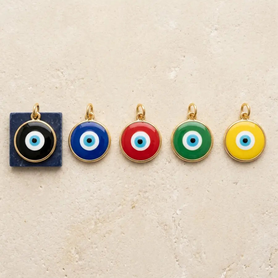 Five identical evil eye charms in black, blue, red, green, and yellow aligned at equal size on ivory stone.