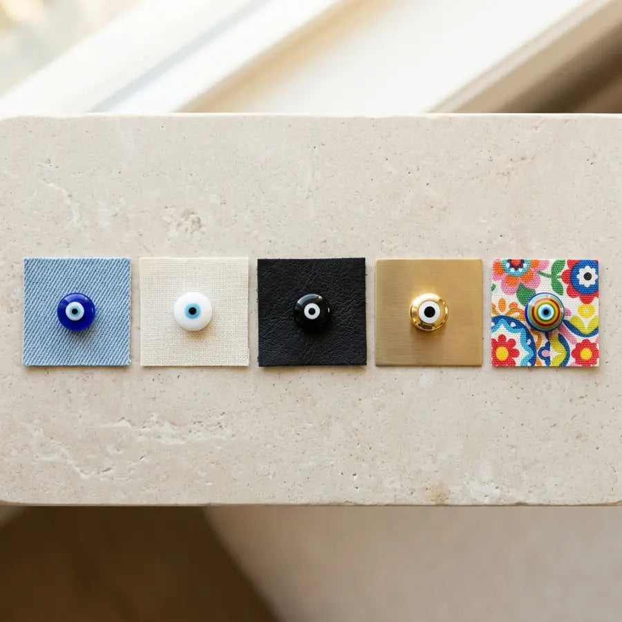 Five evil eye accents in blue, white, black, gold, and multicolor designs on material swatches.