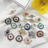 Evil Eye connector charms in oval, almond, Hamsa and floral designs spread across white cloth.