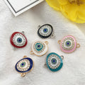 Six oval Evil Eye connector charms in red, black, white, pink, blue and turquoise on white cloth.