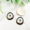 Black oval Evil Eye connectors with gold tone frames, showing decorated fronts and a grooved reverse.