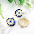 Blue oval Evil Eye connectors with gold tone frames, showing decorated fronts and a grooved back.