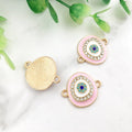 Pink oval Evil Eye connectors with gold tone frames, showing decorated fronts and a grooved back.