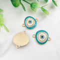 Turquoise oval Evil Eye connectors with gold tone frames, showing decorated fronts and a grooved reverse.
