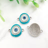 Turquoise oval Evil Eye connectors with silver tone frames, showing decorated fronts and a grooved reverse.