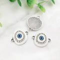 White oval Evil Eye connectors with silver tone frames, showing two decorated fronts and one grooved reverse.