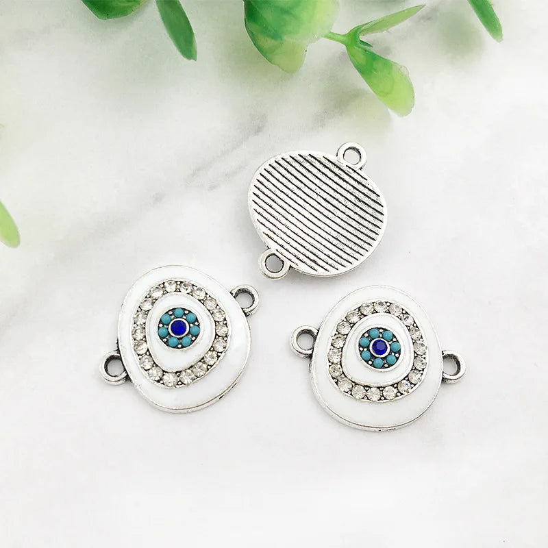 White oval Evil Eye connectors with silver tone frames, showing two decorated fronts and one grooved reverse.