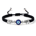 Black cord bracelet with a blue eye between two patterned silver tone elephants