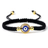 Black knotted cord bracelet with an open gold tone ring around a round blue eye
