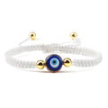 White knotted cord bracelet with one round blue eye and gold tone beads