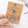 Hand holding a display card with six evil eye bracelets in mixed eye and cord colors