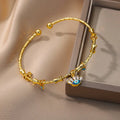 Angled view of a gold tone eyelash eye cuff bracelet beside a display box, with small blue eye charms along the band.