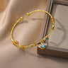 Angled view of a gold tone eyelash eye cuff bracelet beside a display box, with small blue eye charms along the band.