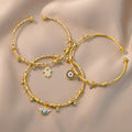 Hamsa hand, eyelash eye and round eye gold tone cuff bracelets spread across beige fabric in an overhead arrangement.