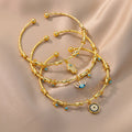 Three gold tone open cuff bracelet styles with Hamsa hand, eyelash eye and round charms overlapping on beige fabric.