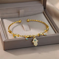 Gold tone cuff bracelet across a display box, with a Hamsa hand charm and small blue eyes hanging over the front edge.