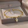 Gold tone cuff bracelet across a display box, with a Hamsa hand charm and small blue eyes hanging over the front edge.