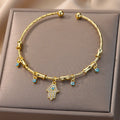 Gold tone Hamsa hand cuff bracelet viewed from above on a beige display cushion, with clear accents and small blue eye charms.