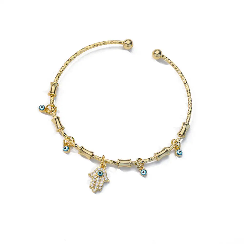 Gold tone Hamsa hand open cuff bracelet on white, with clear accents, a blue eye and four small dangling eye charms.